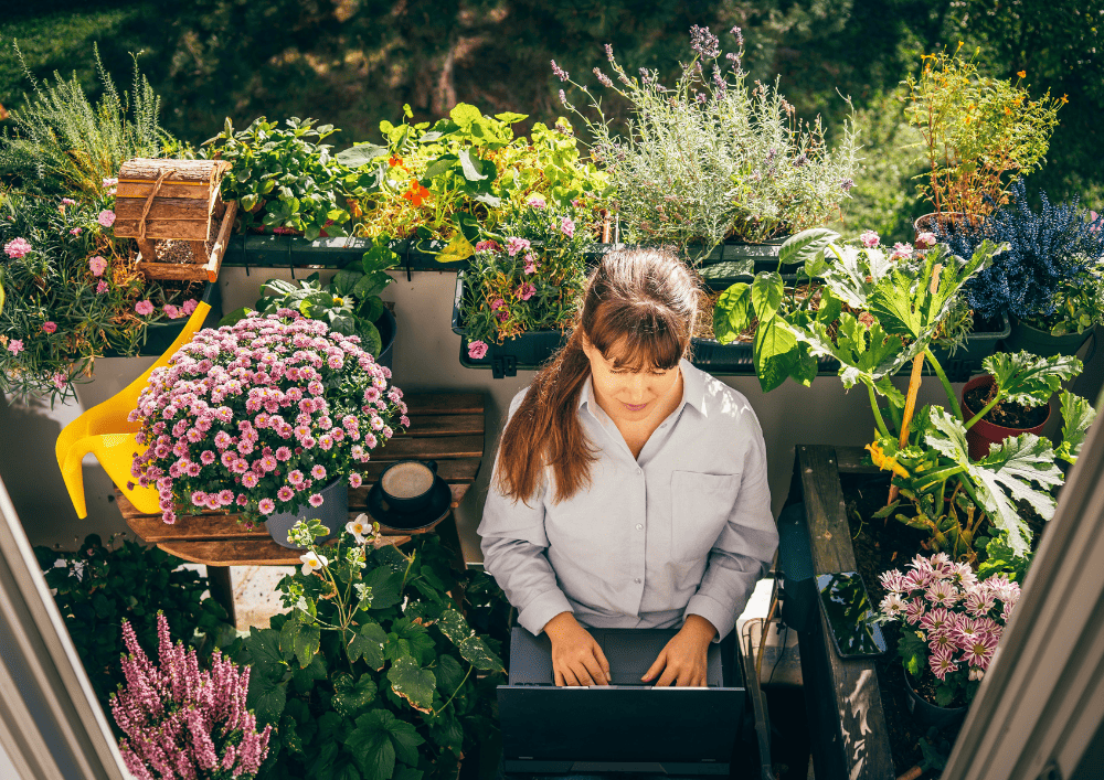 Femme qui travaille sur son ordinateur sur un balcon aménagé et fleuri - jardin urbain comme pièce à vivre